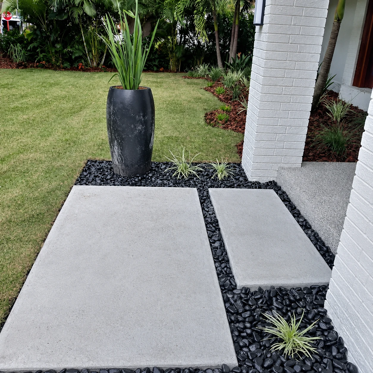 Modern hardscape entry with concrete pavers, black landscape rock, and plant accents.